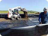 While ridge cap is being fastened and liner trimmed, the Bobcat operator starts to spread screenings above liner.